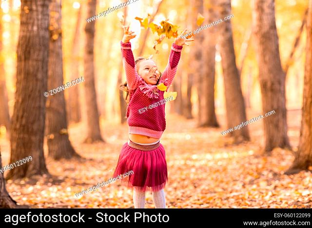 Cute little girl in autumn park throw up orange and yellow color leaves. Fall season