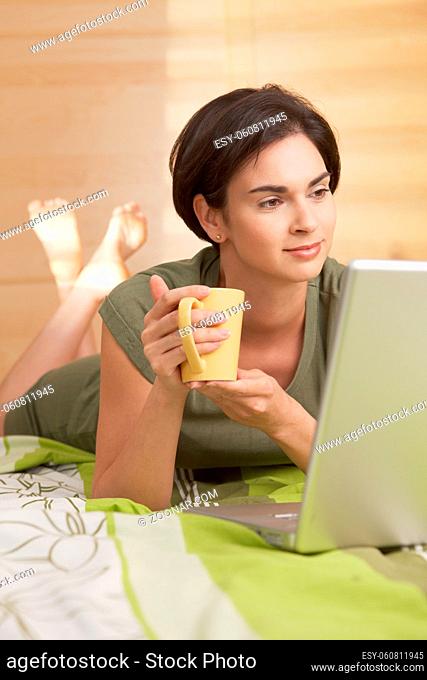 Mid-adult woman having morning coffee in bed, looking at computer