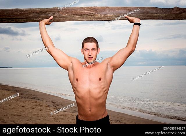 Sport, fitness. Bodybuilder with a big wood on the beach
