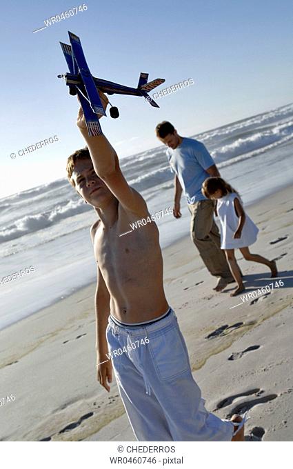 Close-up of a boy holding a model airplane with his father and sister walking behind him