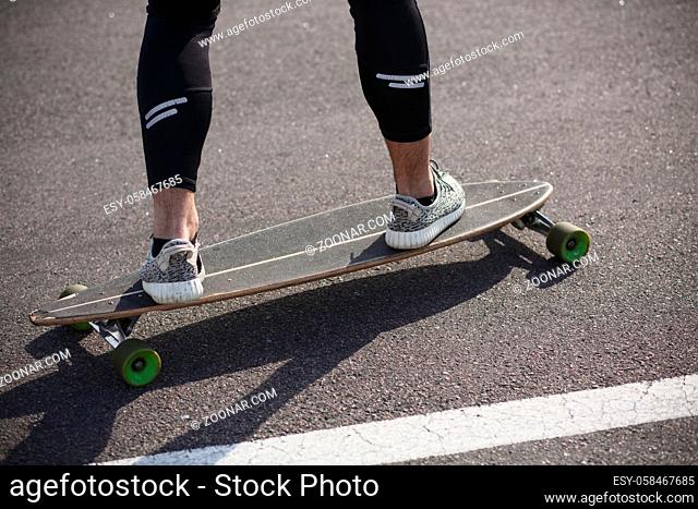 Man riding on longboard skate on road through forest or city. Man#39;s legs on skateboard or longboard