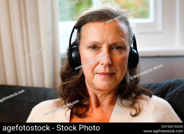 Portrait of happy senior caucasian woman in living room sitting on sofa, wearing headphones