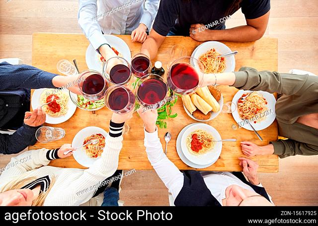 Gruppe Freunde beim Zuprosten mit Glas Wein beim Abendessen mit Spaghetti und Tomatensauce