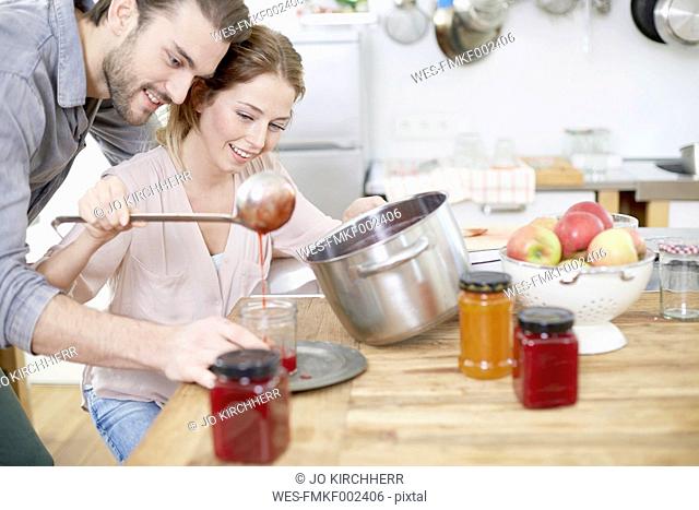 Couple in kitchen filling jam into jars