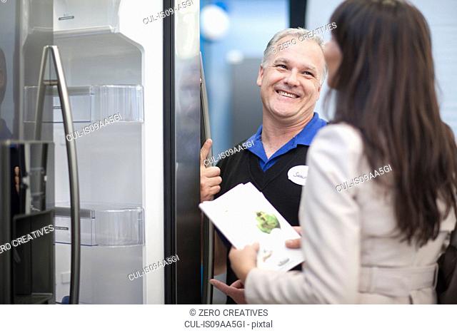 Salesman showing woman fridge in showroom