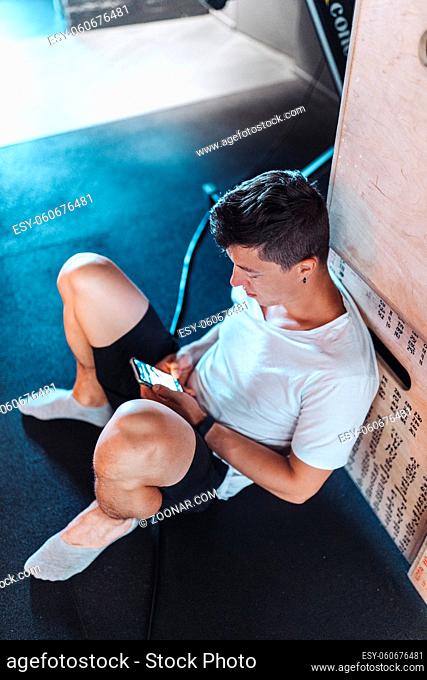 Handsome man using phone while having exercise break in gym. Guy using smartphone after the daily training
