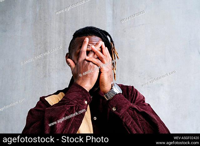 Man covering face with hands in front of wall