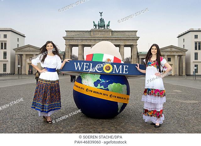 Models Johanna (L) and Klaudia pose in Mexican dresses with an inflatable globe and an oversized sombrero in front of Brandenburg Gate in Berlin, Germany