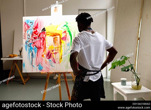 African american male painter at work looking at artwork in art studio