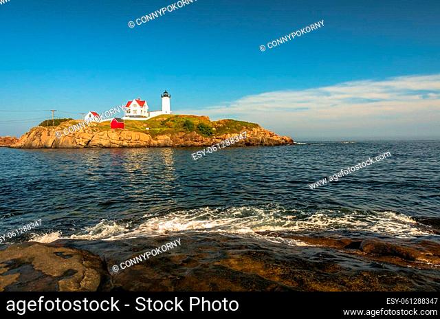 View of the Cape Neddick Lighthouse against blue sky. The Lighthouse, also known as Nubble Light, is located on a small rock island on the Atlantic Ocean in the...