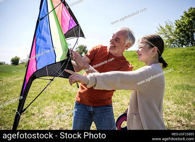 Grandfather guiding granddaughter to fly kite on field