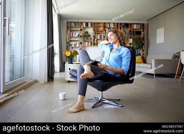 Smiling woman with hands behind head sitting on chair at home