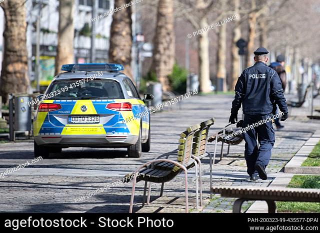 23 March 2020, Saxony, Dresden: A policeman walks beside a police car across the pedestrian passage Hauptstraße. To contain the coronavirus