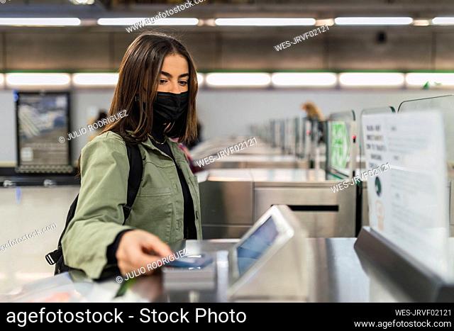 Woman with face mask paying at security barrier in subway
