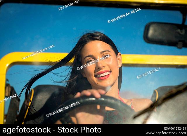 Happy caucasian woman sitting on beach buggy by the sea looking to camera