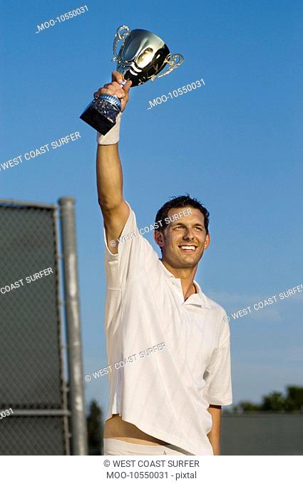 Tennis Player Proudly Holding Trophy in Air