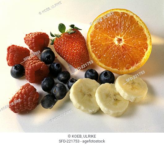 Half an orange, banana slices and various berries
