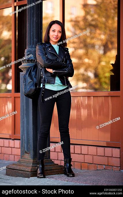 Young fashion woman walking in city street Stylish female model in black leather jacket outdoor