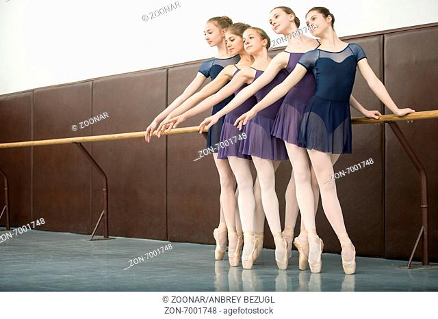 Five ballet dancers in class near the barre. Model wearing white