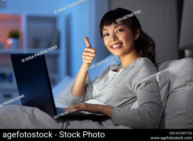 woman with laptop in bed at night shows thumbs up