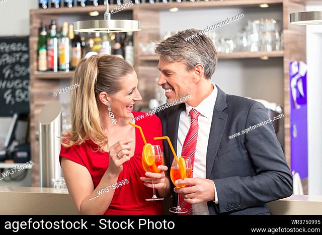 Smiling couple looking each other while holding cocktails