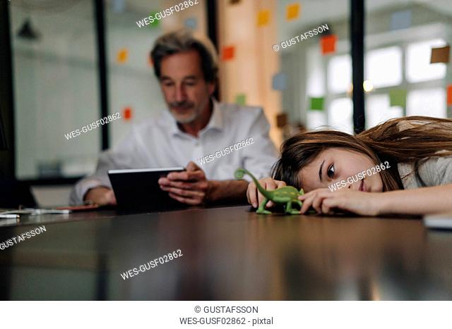 Senior buisinessman using tablet and girl playing with chameleon figurine in office