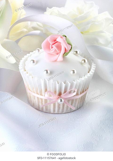 A wedding cupcake with a pink sugar rose and silver balls