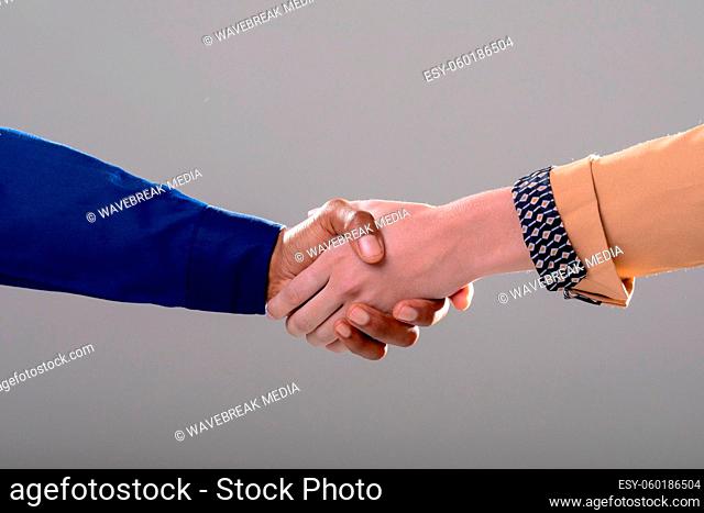 Midsection of caucasian and african american business people shaking hands on grey background