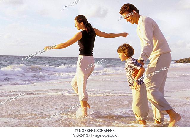 beach-scene, full-figure, dark-haired family with 4 year old daughter is playing bare feeted in the shallow water, all are wearing khaki trousers  - GERMANY