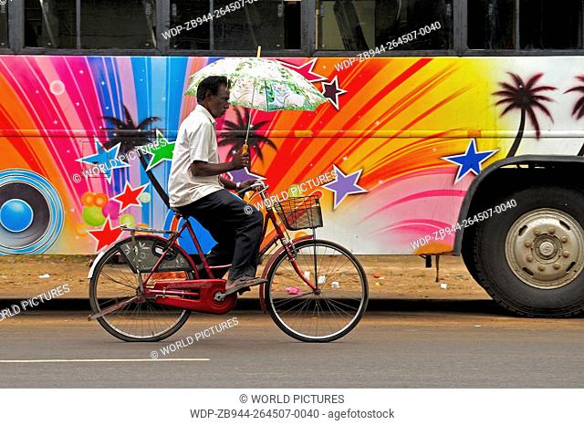 man on a motorcycle with an umbrella with colourful bus, Chidambaram, Tamil Nadu, India