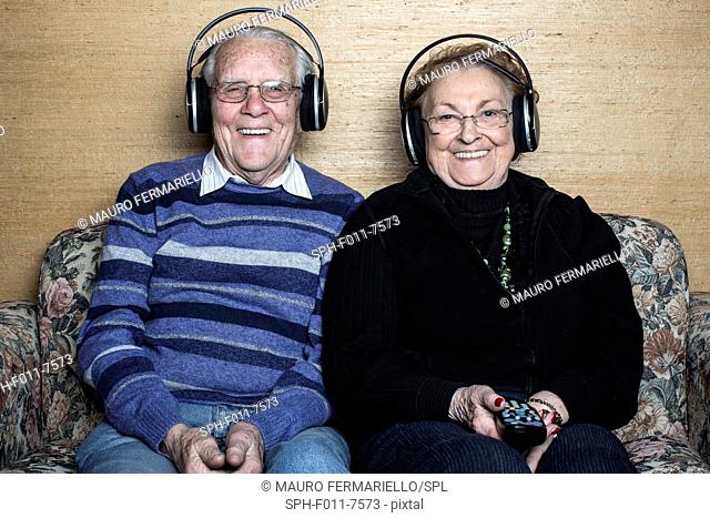 Senior couple sitting on sofa wearing headphones
