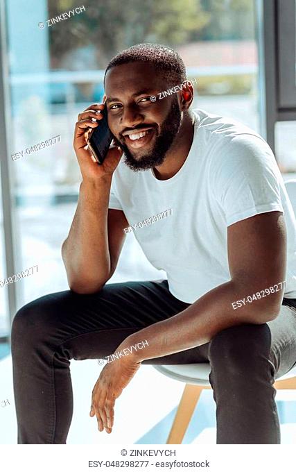 Happy mood. Cheerful young handsome afro american man talking on phone and sharing positivity while feeling happy