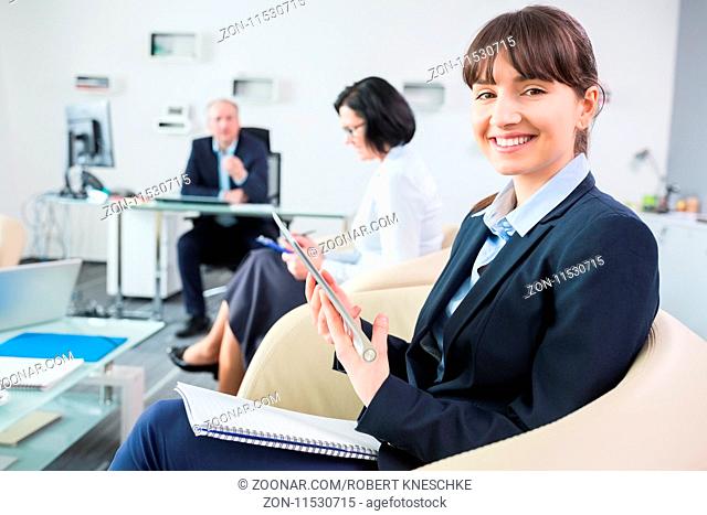 Junge Frau als Business Trainee sitzt mit Tablet Computer im Büro in einem Meeting