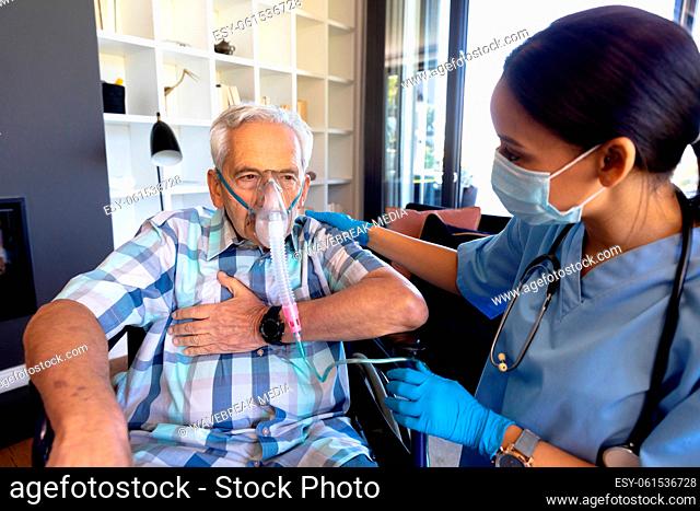 Biracial female health worker helping caucasian senior man to use oxygen mask at home