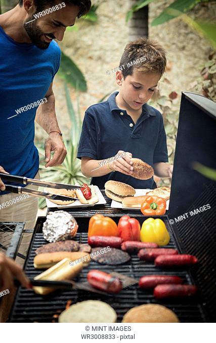 A man and boy standing at a barbecue cooking food