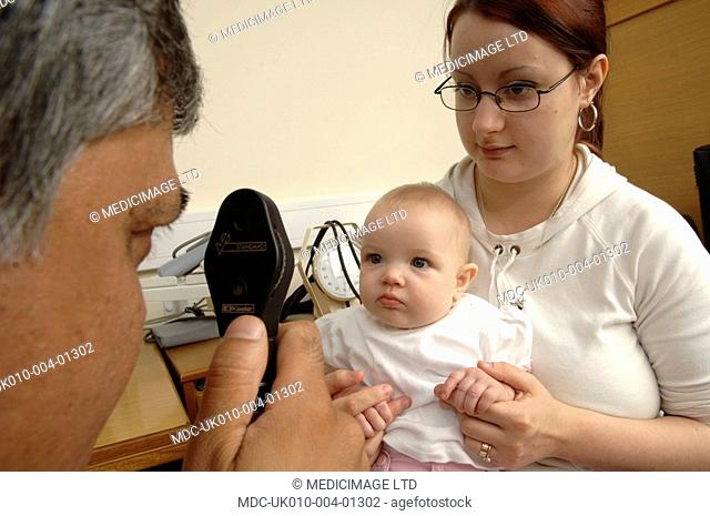 A GP using an ophthalmoscope to examine the health of a baby's retina and vitreous humour
