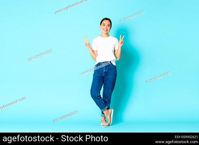 Fashion, beauty and lifestyle concept. Full-length portrait of adorable smiling asian woman in casual outfit, showing peace gestures and looking happy