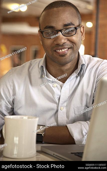 Smiling African American businessman sitting with coffee and laptop