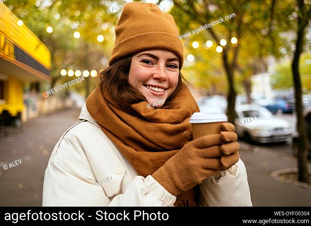 Happy young woman in knit hat with disposable coffee cup during winter