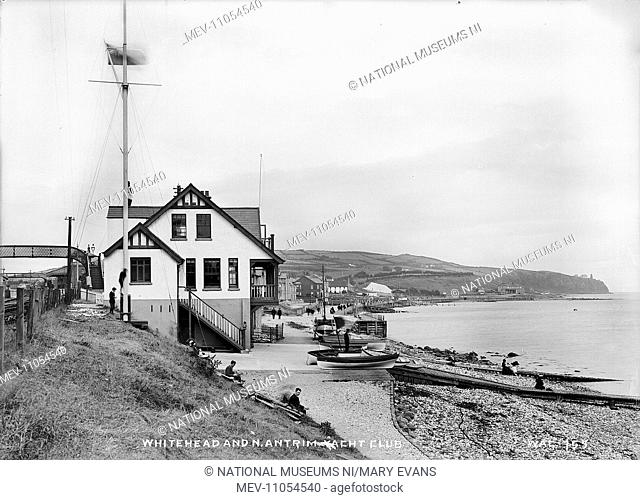 Whitehead and N. Antrim Yacht Club - a view of the building and promenade in the distance. In the foreground are boys and there are boats on the slipways