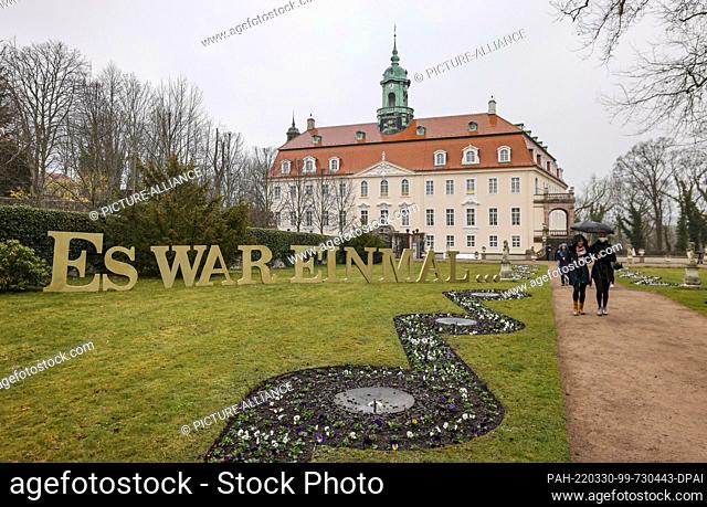30 March 2022, Saxony, Lichtenwalde: Park visitors walk through the park of Lichtenwalde Castle next to the lettering ""Once upon a time...""