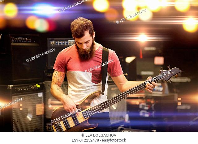 music, people, musical instruments and entertainment concept - male musician with beard playing bass guitar guitar at rock concert or festival over holidays...