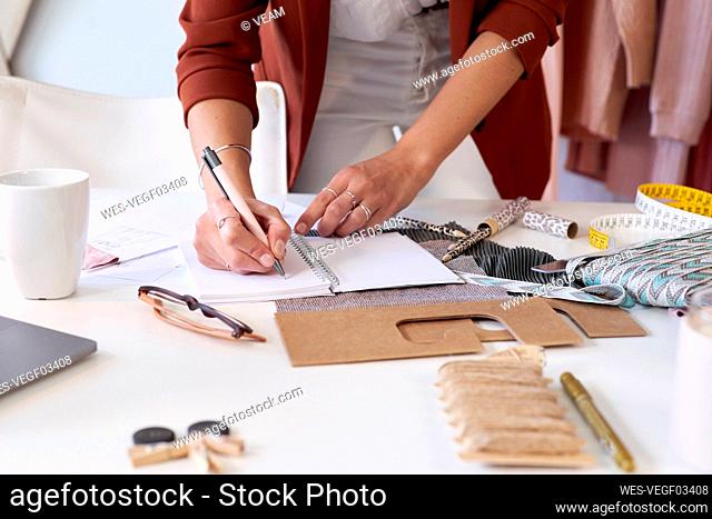 Female fashion professional writing in personal organizer at desk in design studio