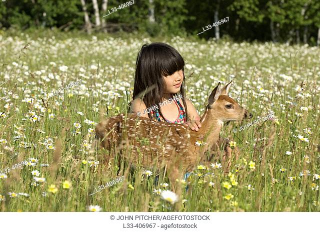 Girl with white tailed deer fawn in field of flowers
