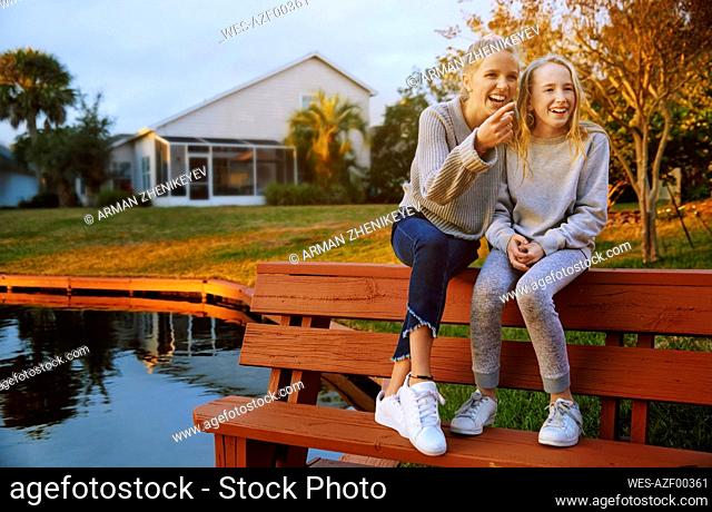 Happy girl gesturing while sitting with friend on bench