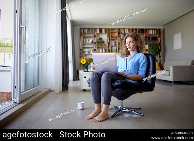 Mid adult woman working on laptop while sitting on chair at home