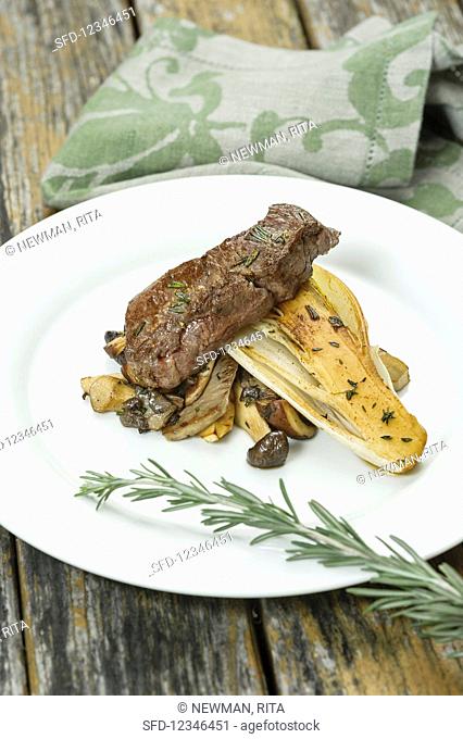 A fried rump steak with chicory and three varieties of mushrooms