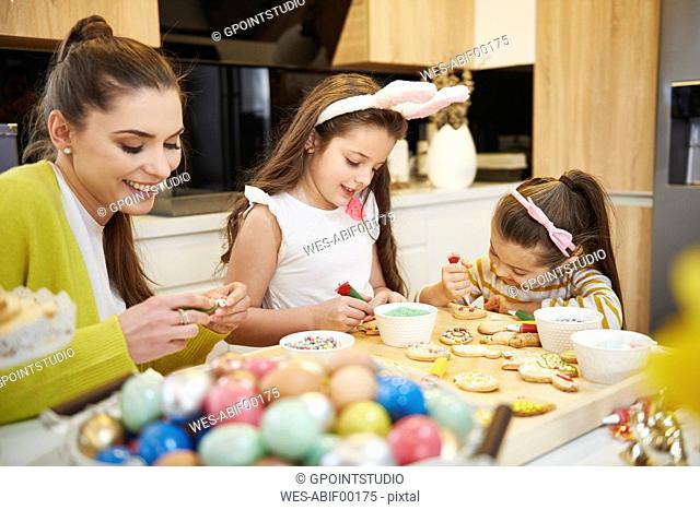 Mother with daughters decorating Easter cookies in kitchen