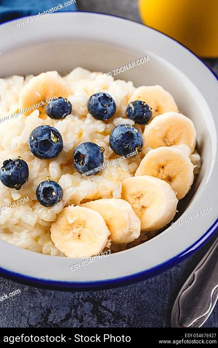 Close up of Milk rice porridge with blueberry and banana, creamy rice pudding or french riz au lait in a metal bowl and enamel mug with tea