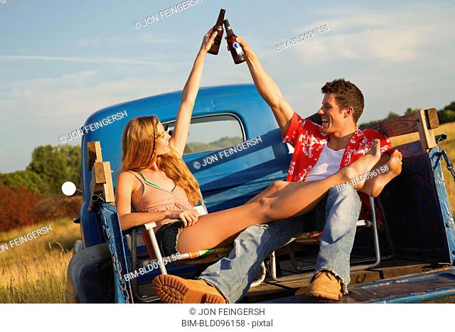 Caucasian couple toasting with beer in back of truck
